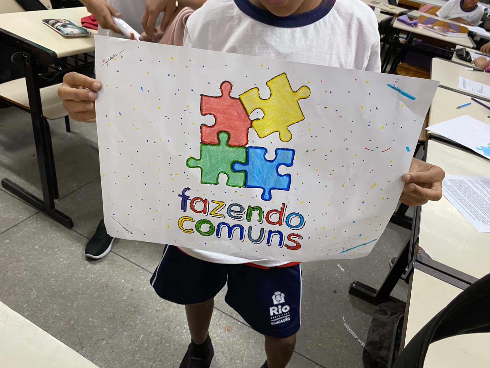 Estudante segurando cartaz ilustrado do projeto Fazendo Comuns na escola